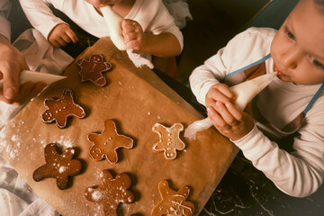 A top view of a black table with gingerbread cookies as a mother and her children decorate them...