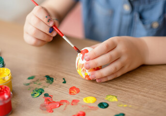 Naklejka premium A child paints a small white egg using bright colors on a wooden table during a creative afternoon activity