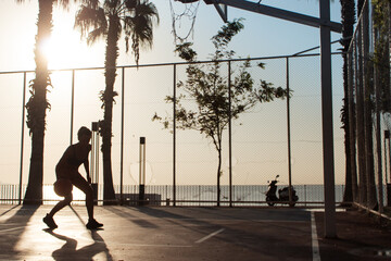silhouette of a sporty woman playing basketball on a basketball court near the sea. outdoor pursuit. healthy lifestyle concept.