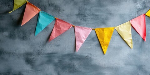Vibrant party flags against a cement gray wall texture background, pastel-colored birthday flags with copyspace. Holiday theme beauty.