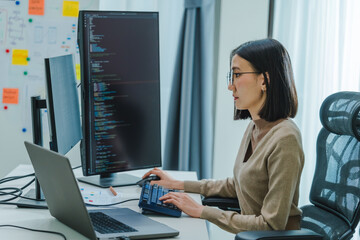 Asian prompt engineer develop coding app with software data sitting in front of computer monitor at...