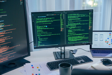 Software development office Workstation setup with multiple monitors displaying code and development diagrams during a nighttime coding session