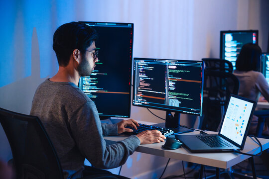 Asian software developers working on multiple screens displaying code and application diagrams at night in modern office