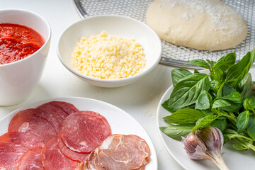Ingredients for making Italian pizza: dough, tomato sauce, parmesan, tomatoes, basil, garlic, sausage on a white table. Real pizza recipe