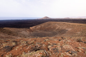 picturesque view of crater of volcano against mountains under light sky in Natural Park of Lanzarote in Canary Islands, Spain, concept of volcanic landscape and wild nature