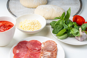 Ingredients for making Italian pizza: dough, tomato sauce, parmesan, tomatoes, basil, garlic, sausage on a white table. Real pizza recipe