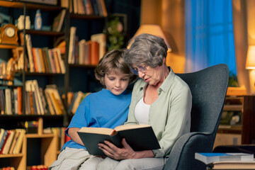 a warm light of living room with library big blue armchair elderly woman sitting with grandson reading book teaching to read
