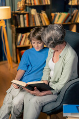 a warm light of living room with library big blue armchair elderly woman sitting with grandson...