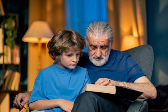 close up a warm light of living room with library big blue armchair grandfather sitting with grandson reading fairy tale hugging grandson