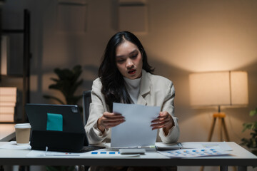 Late Night Focus: A determined businesswoman meticulously reviews documents, working late into the...