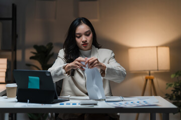 Late Night Crunch: Focused businesswoman meticulously organizing documents at her desk in a dimly...