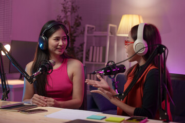 Two beautiful women chat while co-hosting an audio broadcast in a home studio. Recording internet...