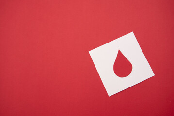 White paper cutout of a blood drop on a red background, blood donation and healthcare concept