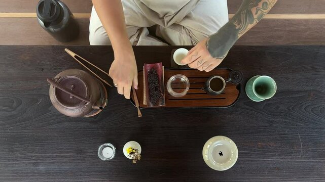 A top view of a Chinese puer tea ceremony on a dark background. Cultural traditions and the art of tea.A man thoughtfully places tea leaves into a teapot.