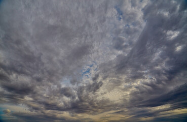 Fototapeta premium Panoramic view of the sky with gray clouds covering it against the backdrop of a sunny horizon, changing weather, sky background.