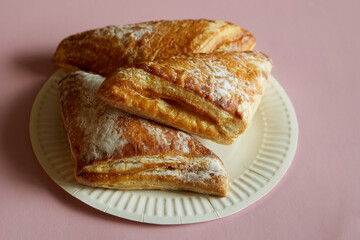 Triangles of puff pastry with sugar sprinkle on a disposable plate on a pink background