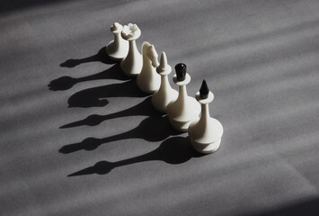 White chess pieces lined up in a single row in sunlight, casting black shadows on a gray...
