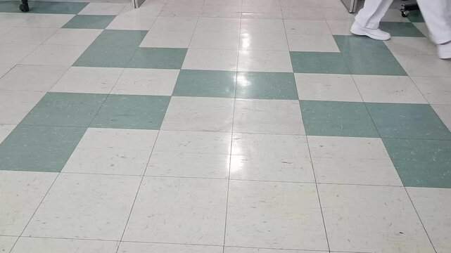 A hospital floor with green and white tiles as patients and doctors walk by in a busy hallway