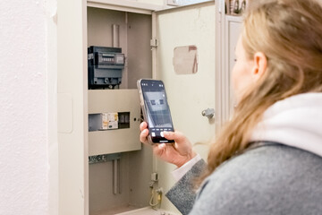 A young woman takes readings from an electric meter for further payment.