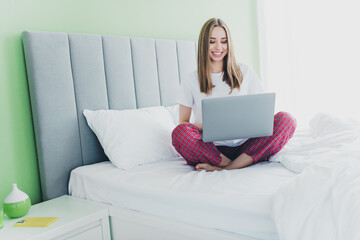 Photo of shiny cute girl nightwear smiling enjoying sitting bed chatting modern device indoors...