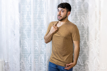 Man pulling on shirt with a hesitant facial expression