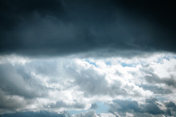 Dramatic sky with dark storm clouds overhead with patches of light and blue sky. The contrast between dark and light areas creates mood and an intense atmosphere.