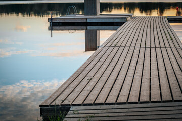 A peaceful lakeside landscape with a wooden pier stretching out into the calm water and reflecting...