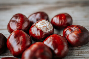 Obraz premium Close-up of shiny brown horse chestnuts displayed on a wooden surface. Their smooth, polished texture and rich brown hues are highlighted in natural light.