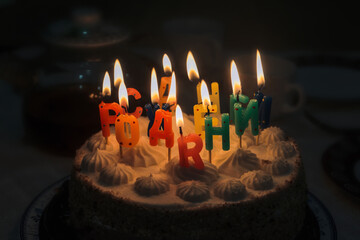 Festive birthday cake with lit candles on a blurred dark background.