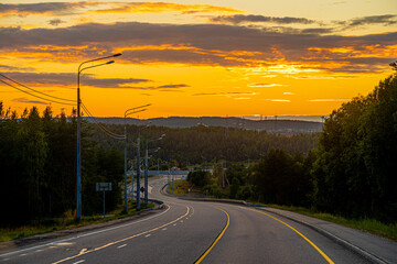 Fototapeta premium photo of road going into sunset, beautiful orange bright sunset sky, road winding along forest, electric poles, marking, trees and forest, road romance