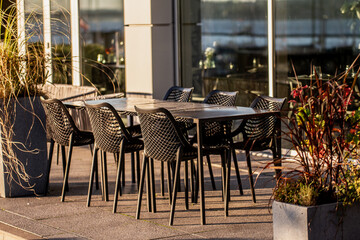 Empty outdoors restaurant tables and chairs for catering to clients and customers in summer next to modern building and water front