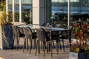 Empty outdoors restaurant tables and chairs for catering to clients and customers in summer next to modern building and water front