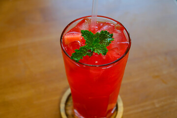 Iced fruit tea or cold watermelon drink in clear glass with mint leaf. Refreshing summer drink. wood background, copy space. 