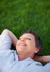 Woman, smile and relax on grass space for comfort, peace and positive mental health. Calm, mature person and happy in nature park for summer travel, freedom and stressless environment for wellness