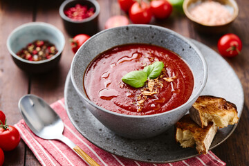 Thick rich Tomato puree Soup garnished with basil leaves and spices in bowl with Grilled Croutons on dark wooden table