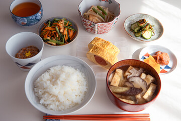 ヘルシーな日本の家庭料理の定食。ご飯・味噌汁・タラコのだし巻き・納豆・小鉢・漬物