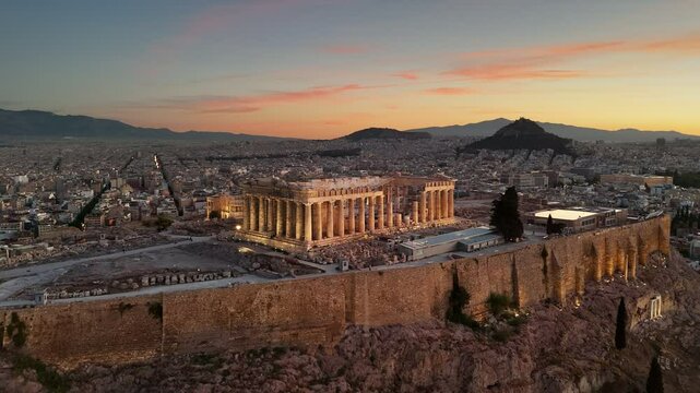 Flying around Parthenon in Athens, Greece at sunrise. Acropolis with city lights and Athens city below. Top international landmark in Greece. Aerial shot, UHD