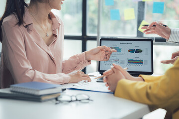 Business Strategy Meeting: A diverse team of business professionals collaborates in a modern office setting, reviewing data and charts on a laptop screen.