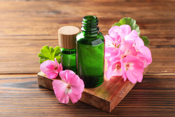 Geranium essential oil in bottles and beautiful flowers on wooden table