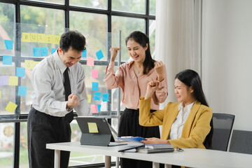 Business Success Celebration:  A team of three diverse professionals celebrates their achievement, with fists raised in victory, showcasing their shared joy and success in a modern office setting.  