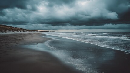 A tranquil beach stretches along the shore, where gentle waves meet the sand. Dark, ominous clouds loom overhead, hinting at an approaching storm during the late afternoon light.
