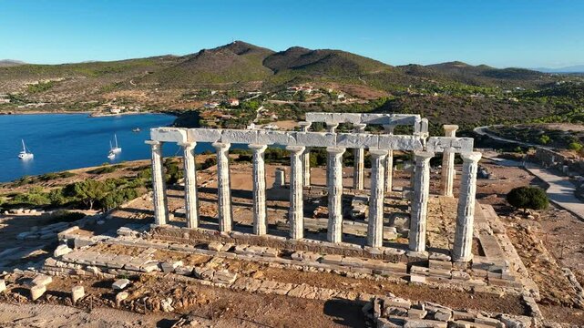 Aerial view of the Temple of Poseidon at sunrise. Temple stands on a cliff at Cape Sounion overlooking the Aegean Sea . Rising sun illuminating the ancient columns and landscape