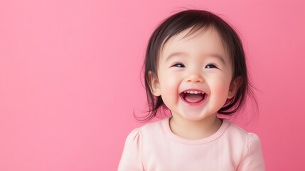 A baby girl with dark hair laughs with her mouth open against a pink background.