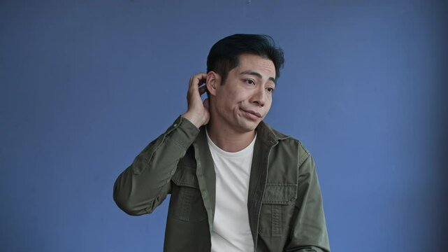 Medium shot of young Asian indifferent male millennial on blue background, copy space