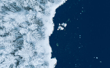 Aerial view of blue water sea and snow covered trees woods in winter Finland.