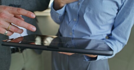 The car dealership manager shows the tablet screen to the customer while standing in the showroom. Close-up of their hands, unrecognizable person