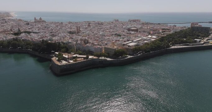 Aerial drone wide cityscape of C&aacute;diz in Spain, Andalusia, Europe, on bright sunny day, facing San Sebastian castle fortress and lighthouse and Baluarte de la Candelaria. Shot in 5K ProRes 422 HQ