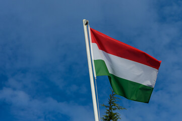 Hungarian flag fluttering against a bright blue sky with clouds, showcasing national pride in a picturesque outdoor setting