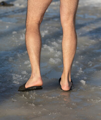 A man is standing in the snow with his feet in the water