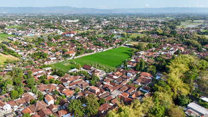 Aerial perspective captures a peaceful suburb featuring houses and green fields under clear skies